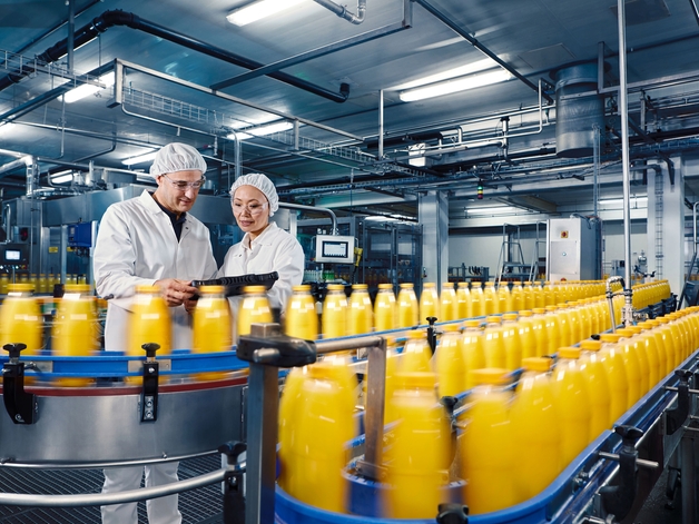 Dva inženýři v továrně na nápoje dohlížející na proces plnění pomerančového džusu.